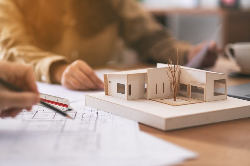 Group of an architect working and discussing about an architecture model together with shop drawing paper on table in office